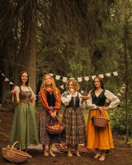 Gruppe festlich gekleideter Frauen im Auenland-Stil bei einem Picknick im Wald